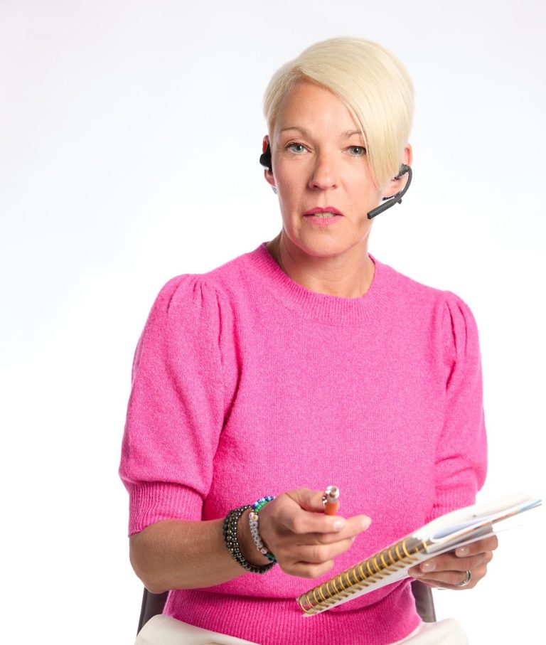 Therapiegespräch vereinbaren. Nadja Hummer trägt e Headphone und spricht Sie mit direktem Blick in die Kamera an. Sie trägt einen pinkfarbenen Pullover, eine weiße Hose.