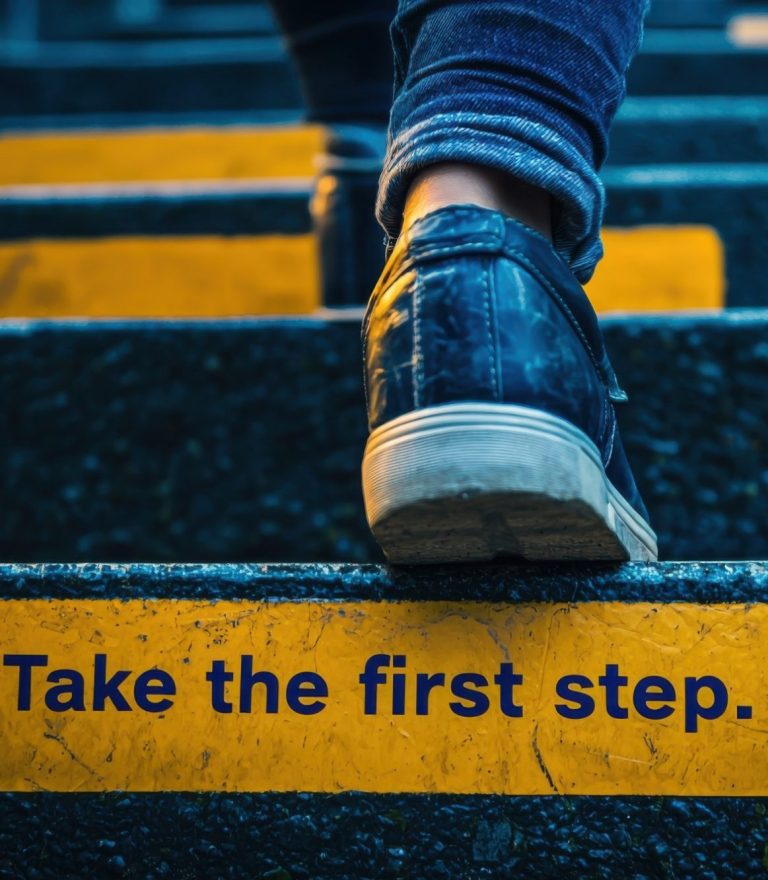 Jemand geht die Treppe nach oben. Auf einer Stufe steht "Take the first step." Die Person ist dabei den Weg in die richtige Richtung gehen.