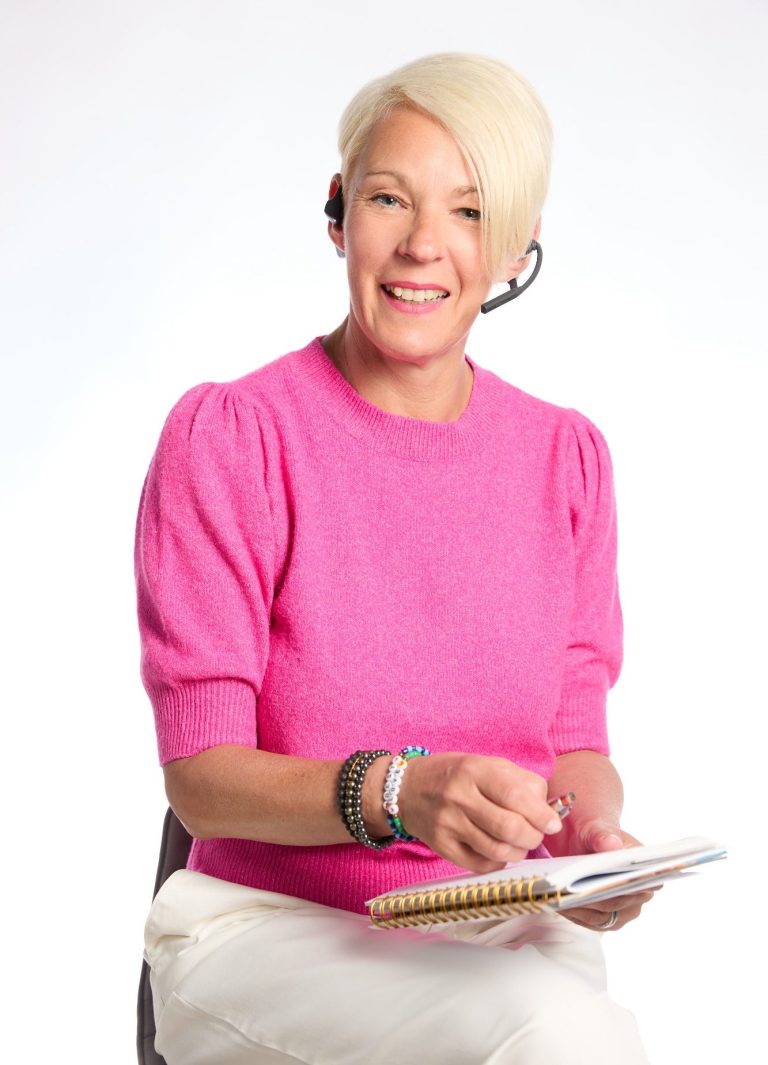 Therapiegespräch vereinbaren. Nadja Hummer trägt e Headphone und spricht Sie mit direktem Blick in die Kamera an. Sie trägt einen pinkfarbenen Pullover, eine weiße Hose.