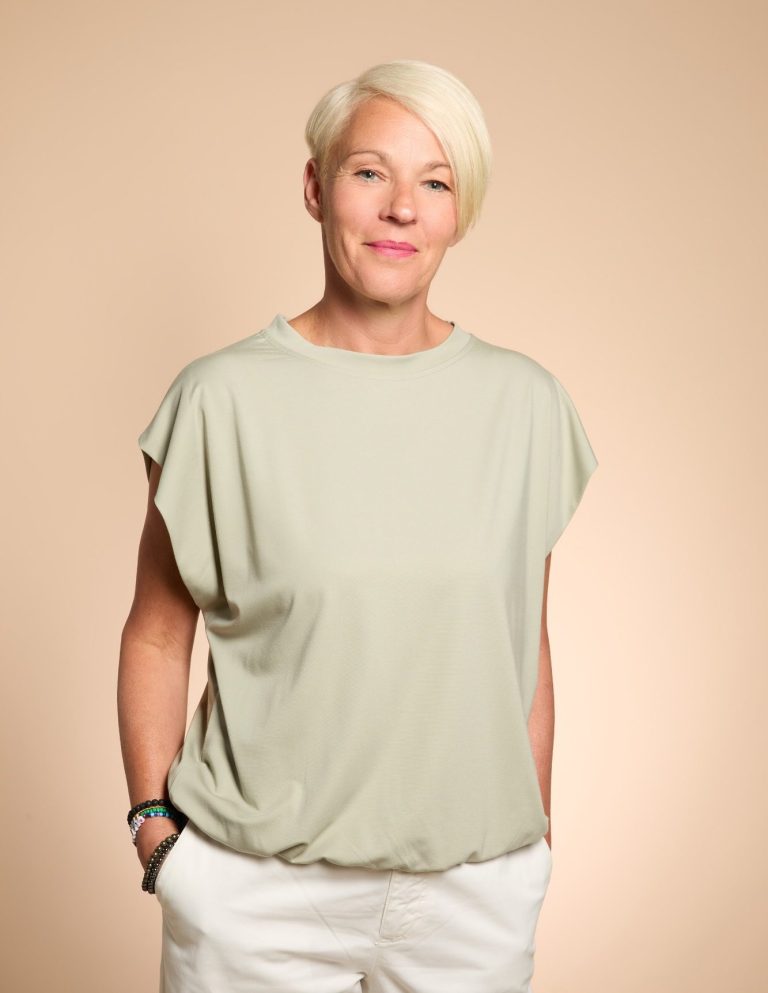Nadja Hummer schaut in die Kamera und lächelt sie auffordernd an. Sie hat ein hellgrünes T-Shirt und eine weiße Hose an. Der Blick ist offen